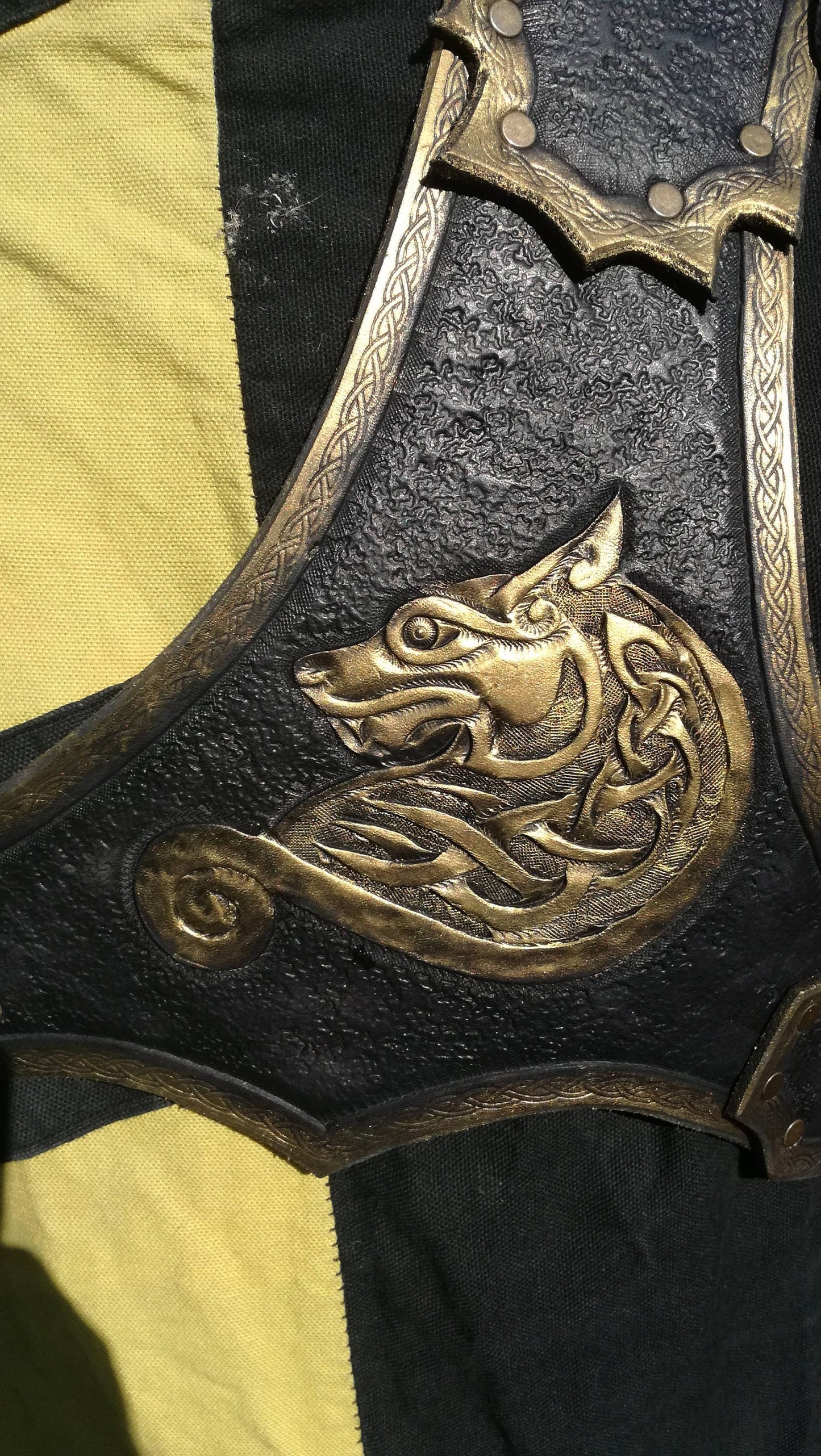 A handcrafted black and gold leather spaulder featuring an intricate engraved wolf design. Made from high-quality Italian vegetable-tanned leather, this shoulder armor is designed for warriors, knights, and adventurers. The overlapping plates provide excellent flexibility, while the secure double-strap system ensures a comfortable fit. Fully customizable with engraving, color, and size options, this pauldron is perfect for LARP, cosplay, and medieval fantasy costumes